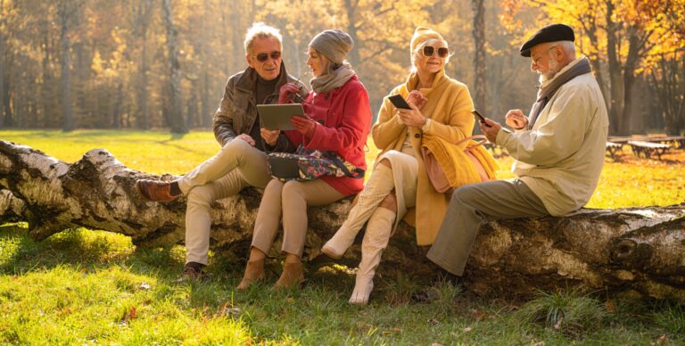 Starsi ludzie korzystający z telefonów komórkowych i tabletów w jesiennym parku
